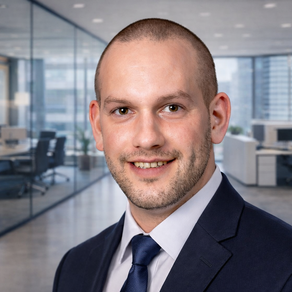 Smiling bald man wearing a navy suit, white shirt, and navy tie in a modern office setting.
